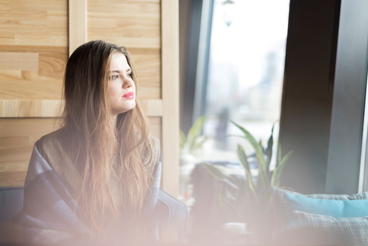 Frau steht ruhig am Fenster und reflektiert über Beziehungen und Selbstrespekt