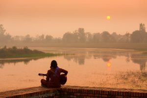 Person sitzt ruhig am See bei Sonnenuntergang und findet inneren Frieden.