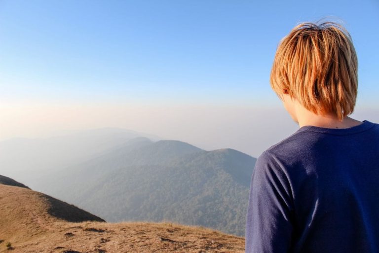 Person steht entschlossen auf einem Hügel bei Sonnenaufgang und blickt nach vorne.