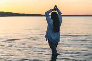 Person blickt hoffnungsvoll auf einen Sonnenaufgang am Meer.