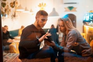 Person nutzt KI-Chatbot während echte soziale Interaktion im Hintergrund stattfindet