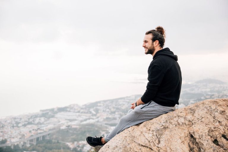 Silhouette eines Mannes, der auf einem Felsen steht und mit erhobenen Armen in den Himmel blickt.