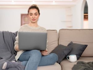 Eine junge Frau sitzt mit Laptop auf dem Sofa und führt ein Online-Gespräch.