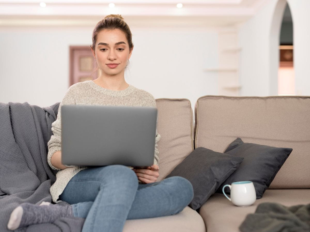 Eine junge Frau sitzt mit Laptop auf dem Sofa und führt ein Online-Gespräch.